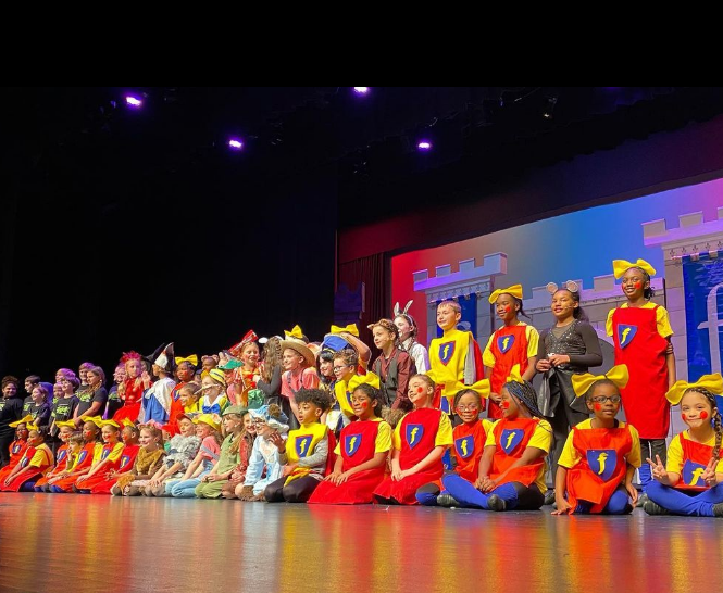 The student cast of Shrek Jr in costume on stage posing for a photo